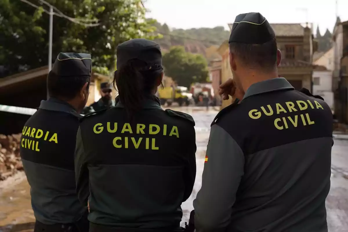 Tres agentes de la Guardia Civil de espaldas observan una escena en un entorno urbano.