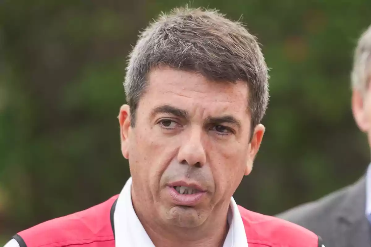 Un hombre con cabello corto y canoso lleva un chaleco rojo y blanco mientras está al aire libre.