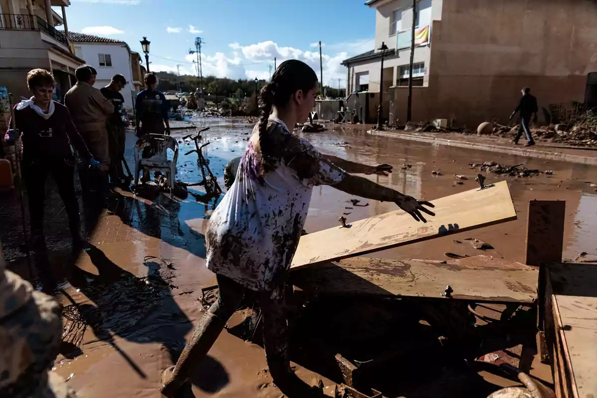 Personas colaboran en la limpieza de una calle cubierta de lodo tras una inundación.