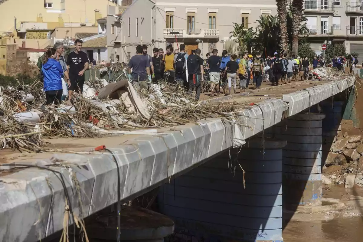 Personas caminando sobre un puente cubierto de escombros y ramas después de una inundación en un área urbana.