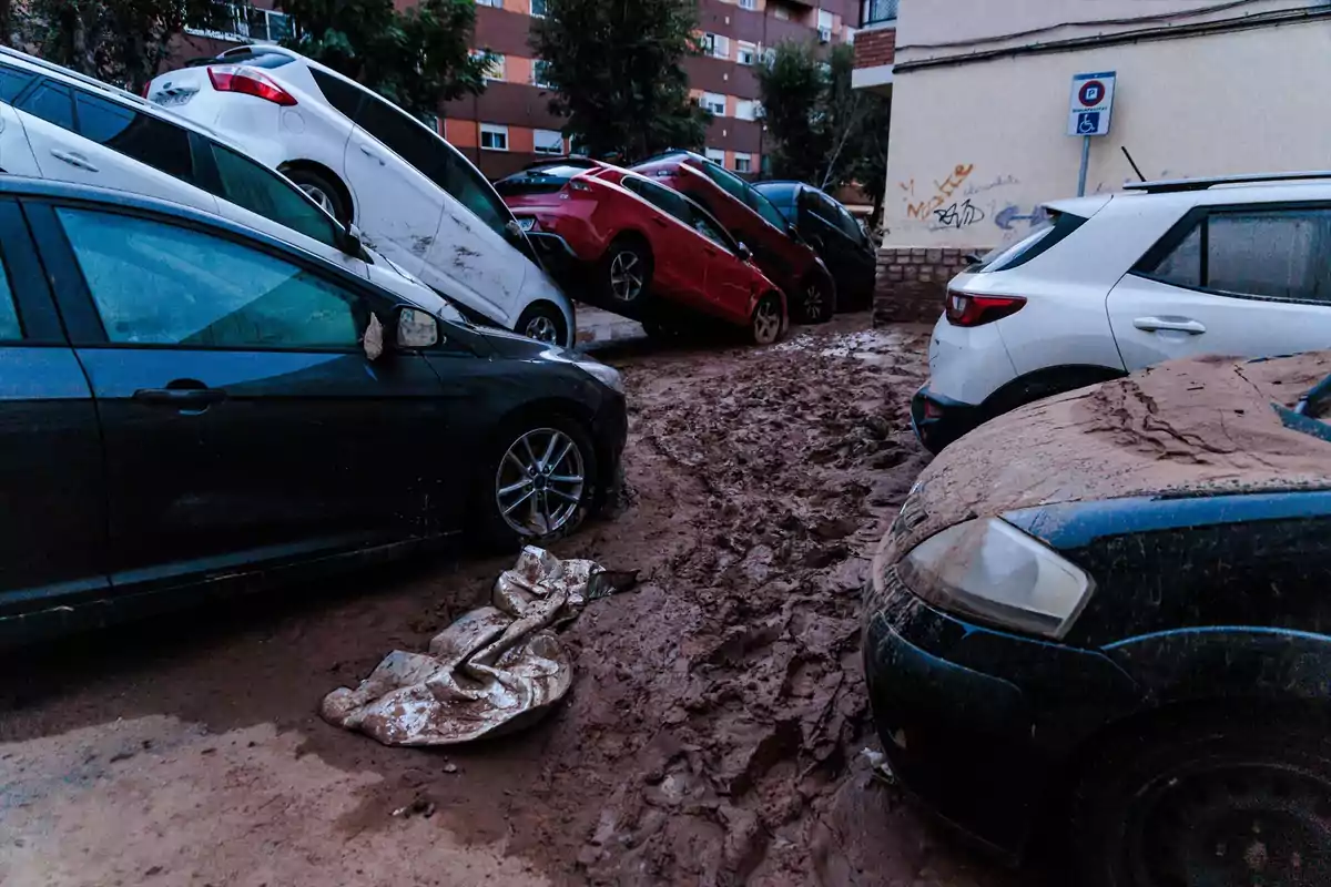 Coches apilados y cubiertos de barro tras una inundación en una zona urbana.