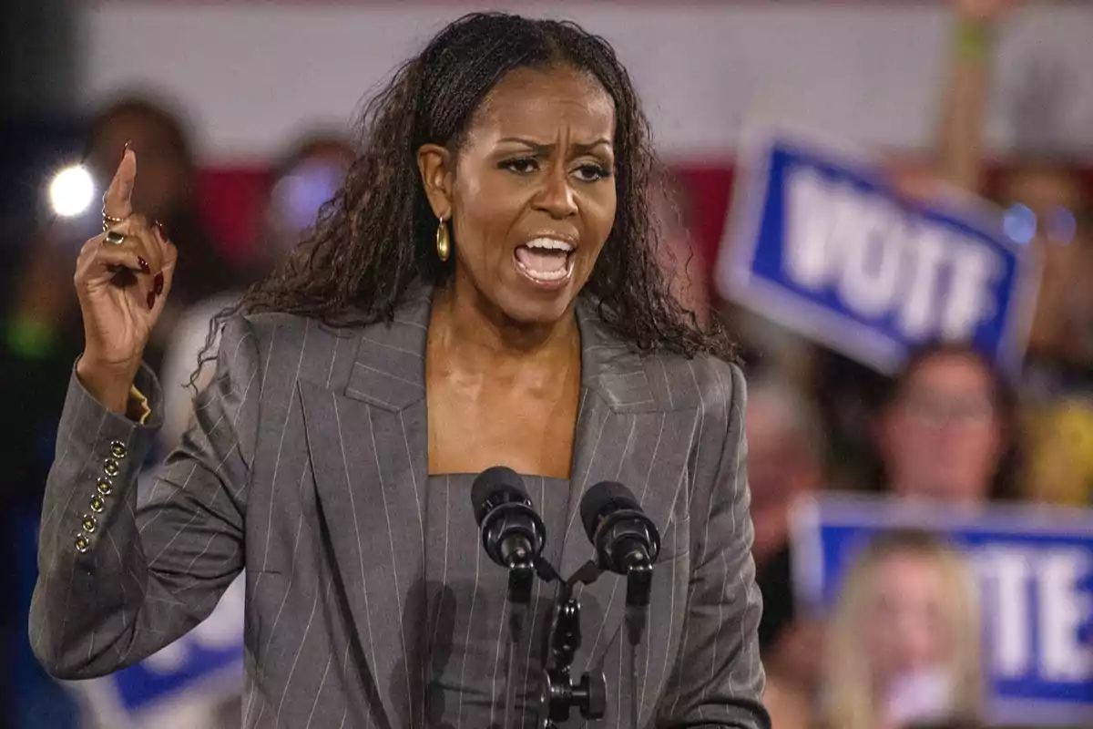 A woman speaking at a rally with microphones in front of her and people holding A woman speaking at a rally with microphones in front of her and people holding