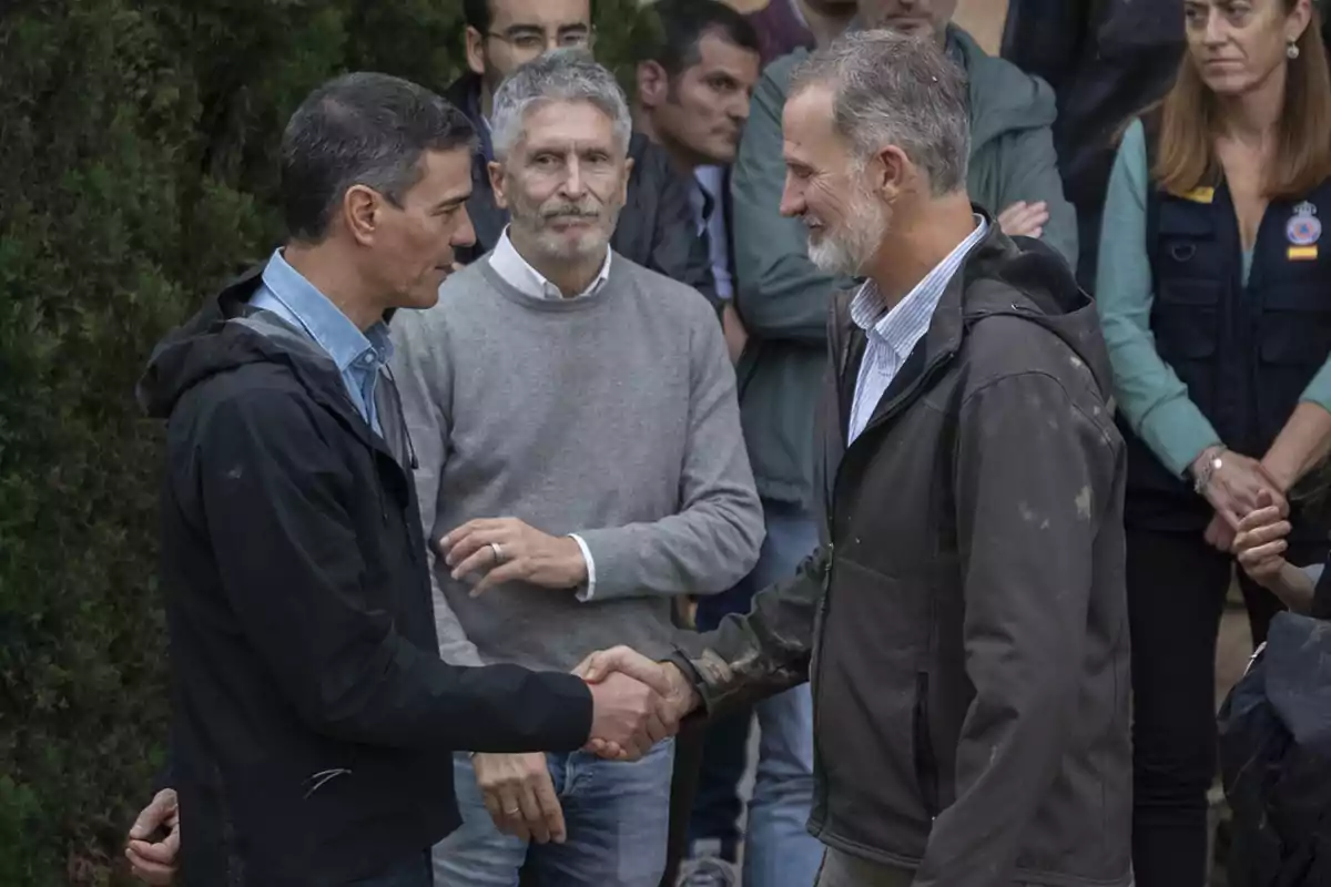 Dos hombres se dan la mano mientras otras personas observan en el fondo.