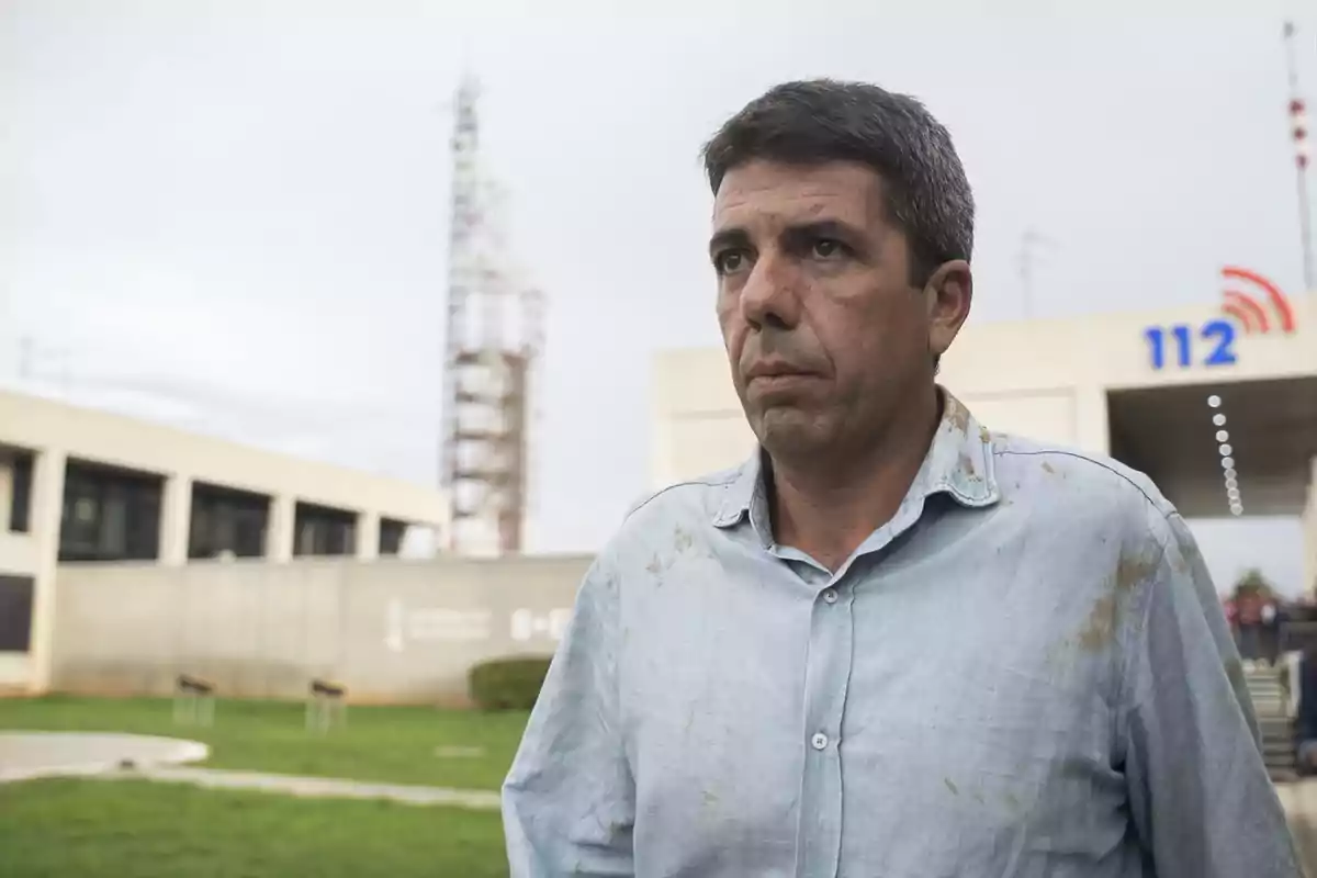 Un hombre con camisa azul manchada está de pie frente a un edificio con el número 112 visible en el fondo. Un hombre con camisa azul manchada está de pie frente a un edificio con el número 112 visible en el fondo.