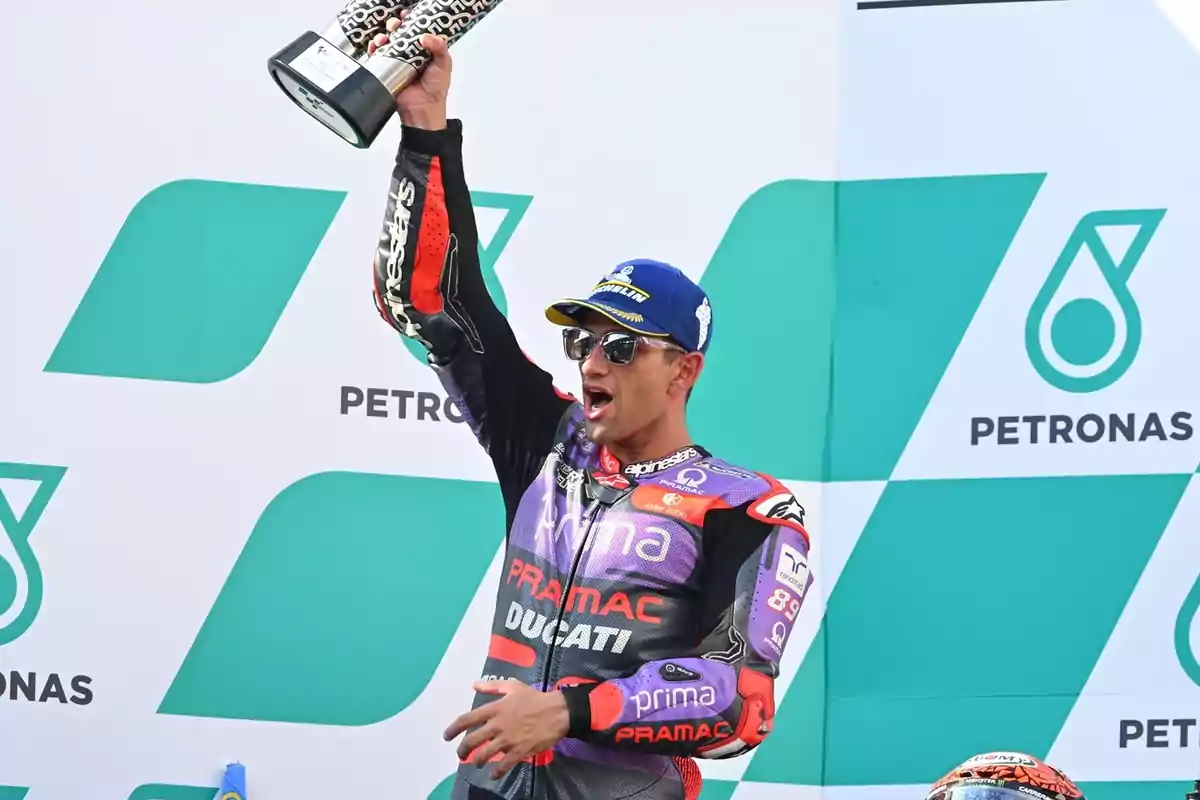 Un piloto de motociclismo celebra levantando un trofeo en el podio.