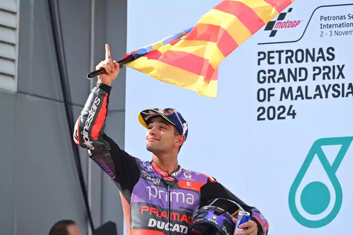 Un piloto de motociclismo celebra sosteniendo una bandera en el podio del Gran Premio de Malasia 2024.