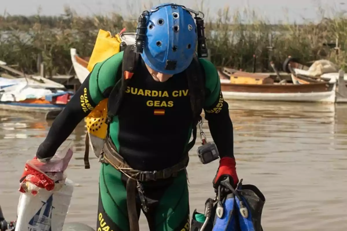 Un buzo del grupo de actividades subacuáticas de la Guardia Civil con equipo de buceo y casco azul junto a un cuerpo de agua.