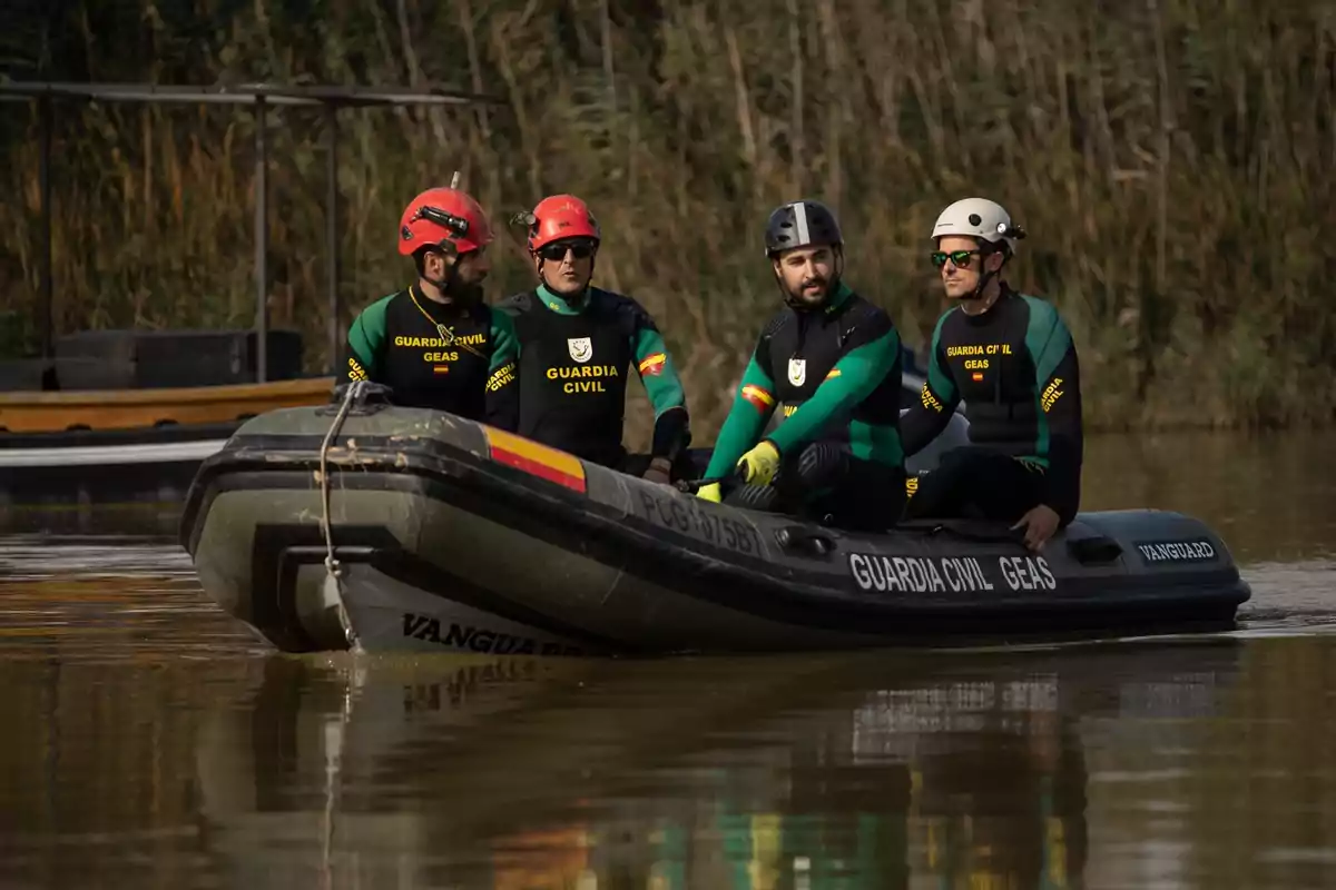 Un grupo de cuatro personas con trajes de la Guardia Civil y cascos están en una lancha inflable en un cuerpo de agua rodeado de vegetación.