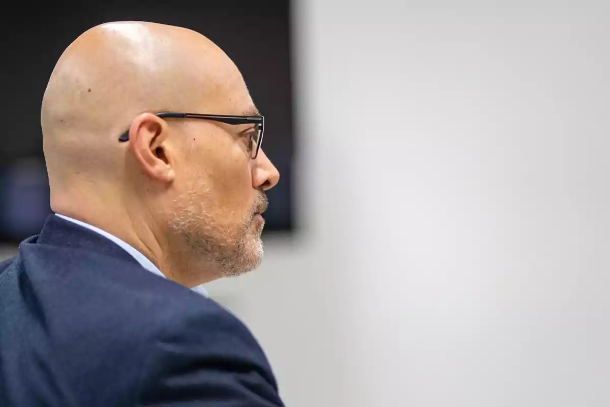 Hombre calvo con gafas y barba de perfil en un entorno profesional.