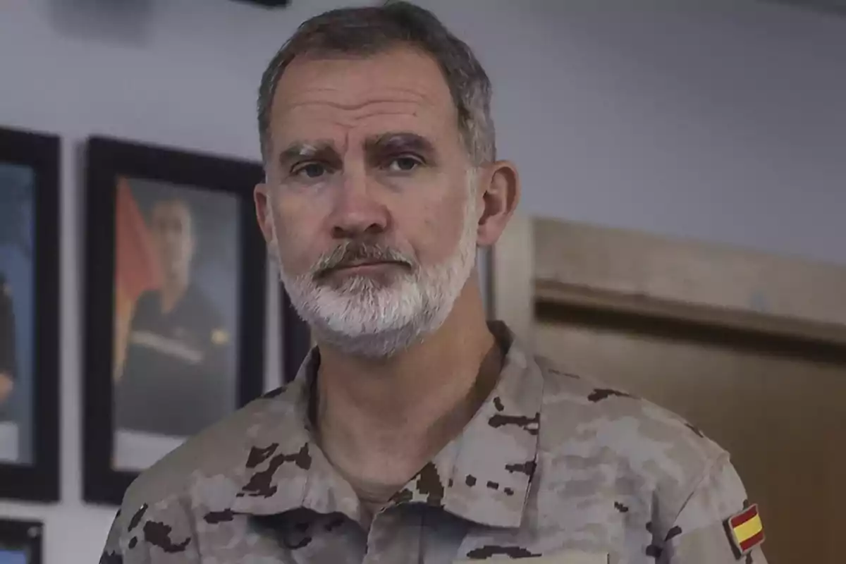 Hombre con uniforme militar camuflado y barba blanca en una habitación con retratos en la pared.