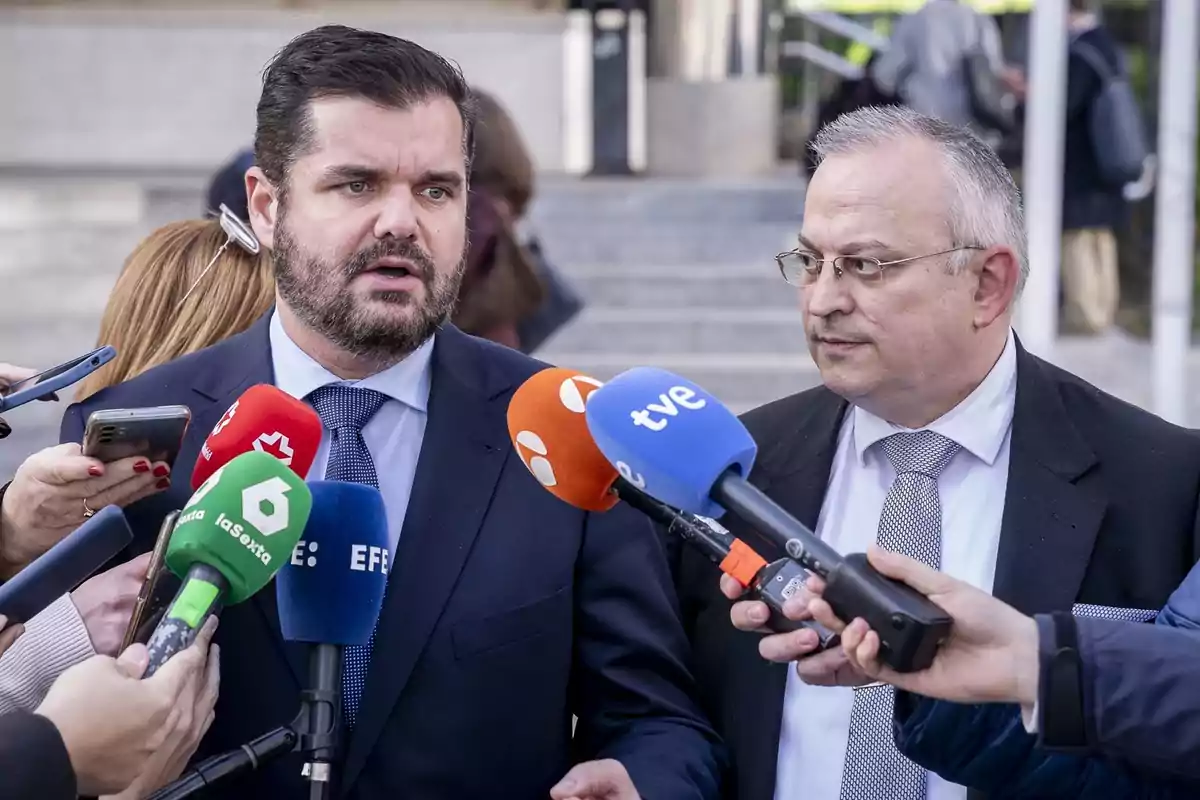 Dos hombres en traje son entrevistados por varios medios de comunicación, rodeados de micrófonos de diferentes cadenas.