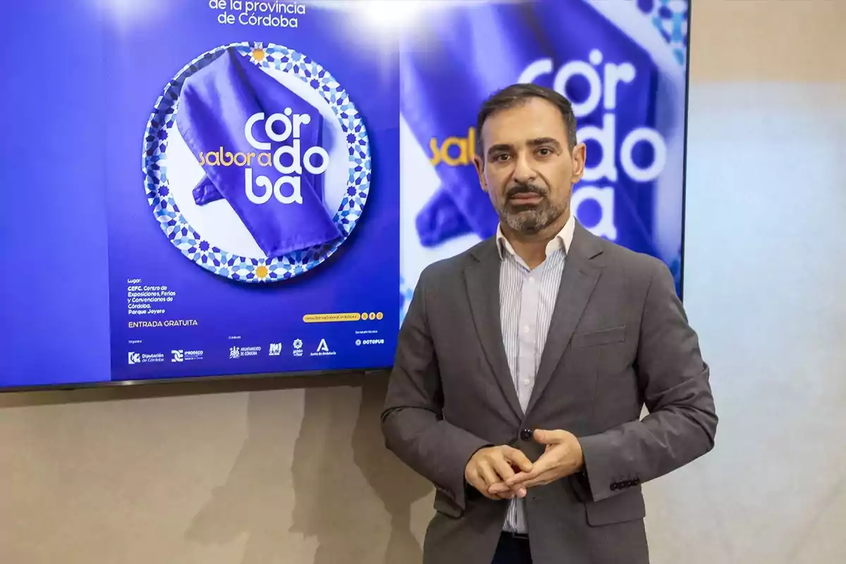 Un hombre de traje está de pie frente a un cartel que promociona un evento llamado "Sabor a Córdoba".