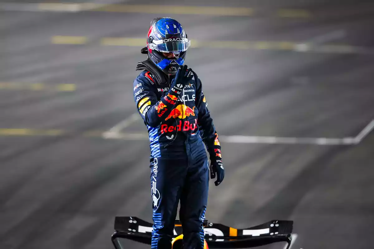 Piloto de carreras con casco y traje de Red Bull en una pista de carreras.