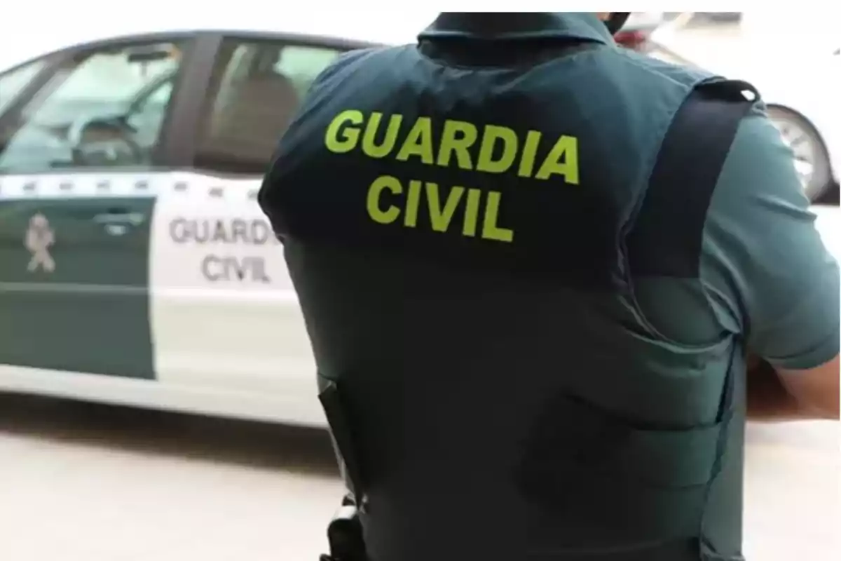 Un agente de la Guardia Civil de espaldas con un coche patrulla al fondo.