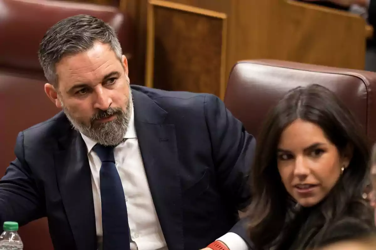 Two people seated in a formal setting, possibly in a meeting or conference.