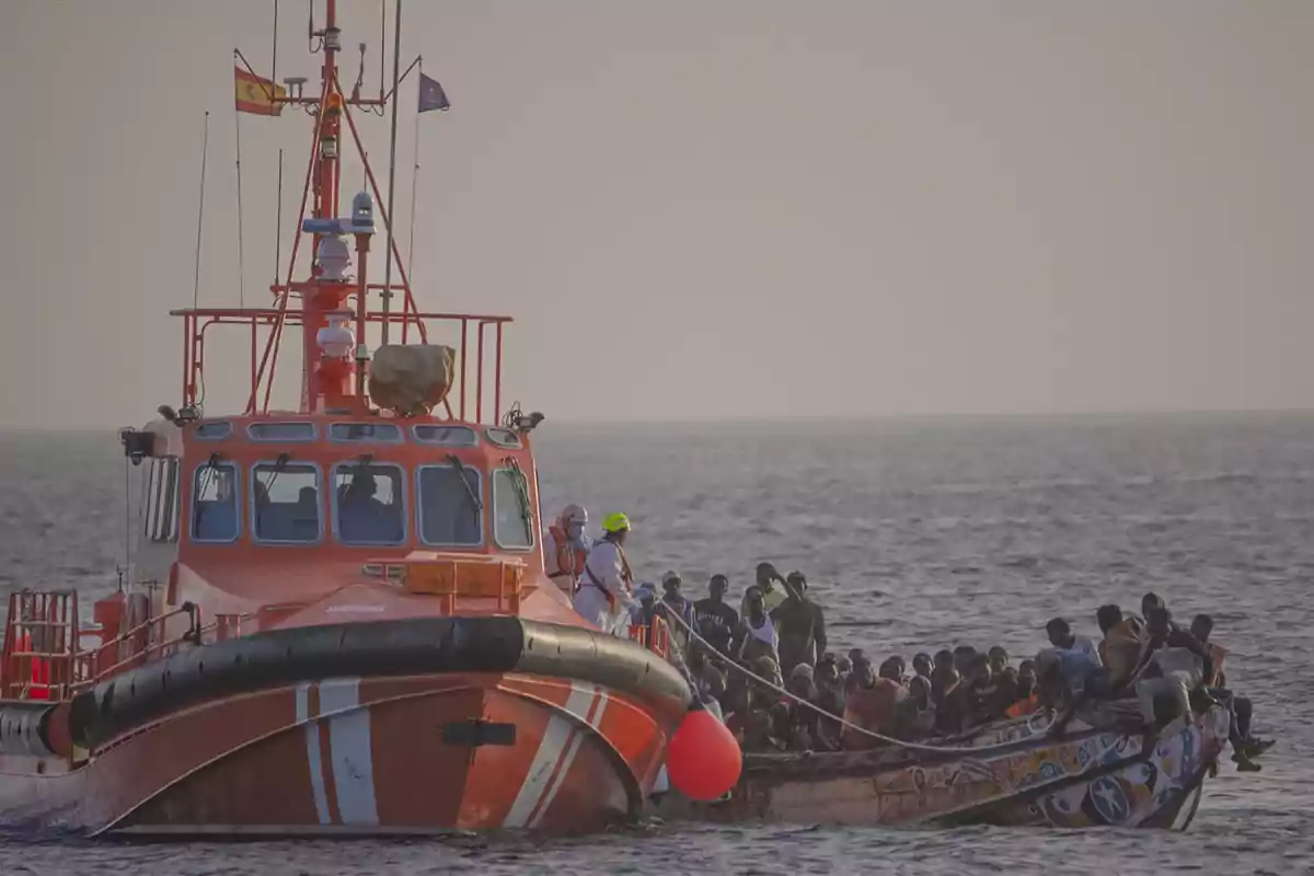 Una embarcación de rescate se encuentra junto a un bote lleno de personas en el mar.