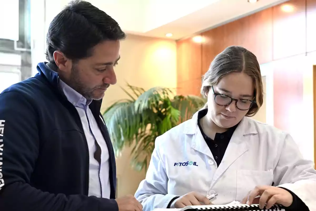 Dos personas revisan documentos en un entorno de oficina, una de ellas lleva una bata blanca.