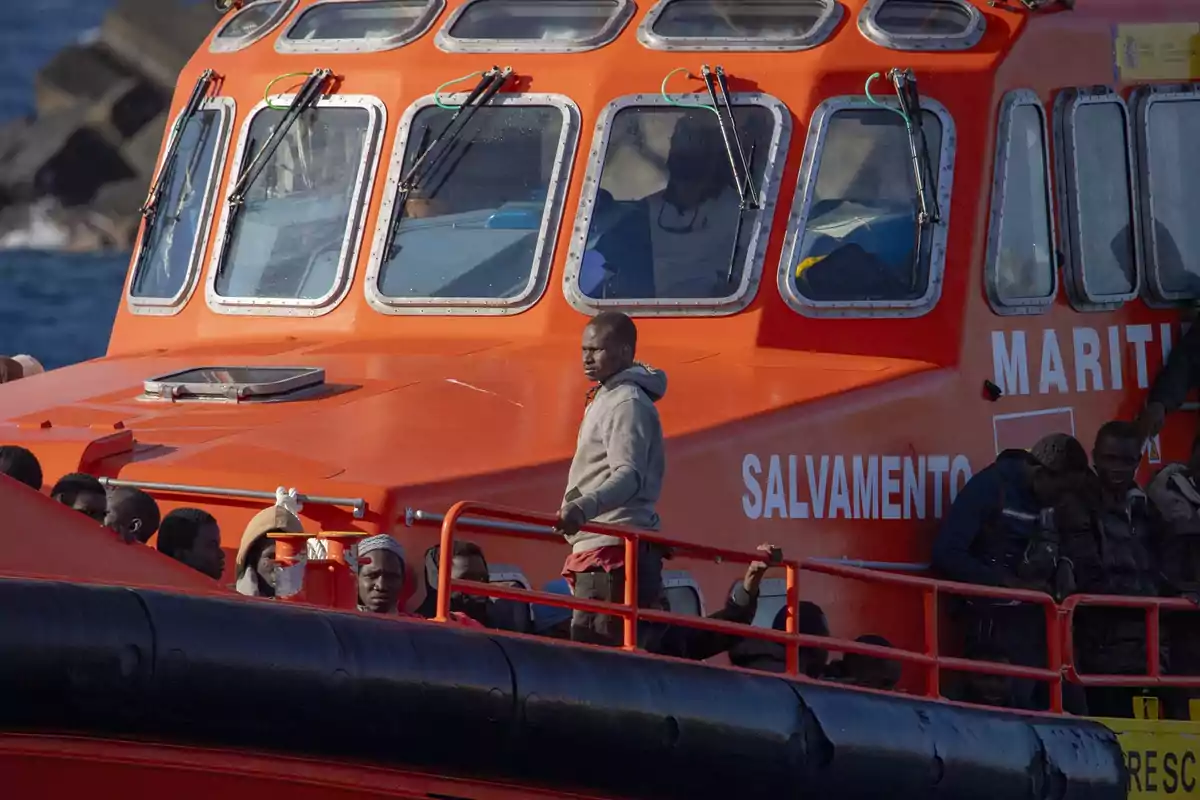 Un grupo de personas migrantes viaja en un barco de salvamento marítimo de color naranja