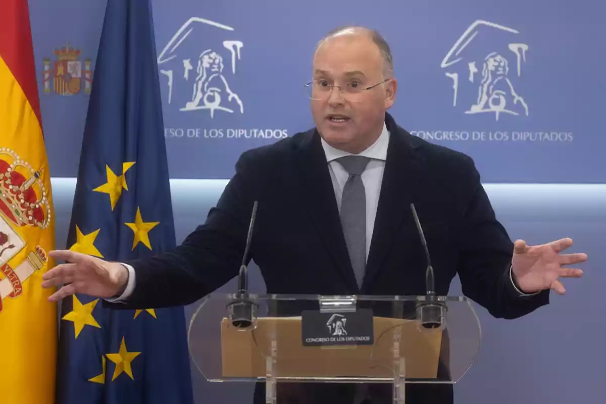 Un hombre hablando en un podio frente a banderas de España y la Unión Europea en el Congreso de los Diputados.