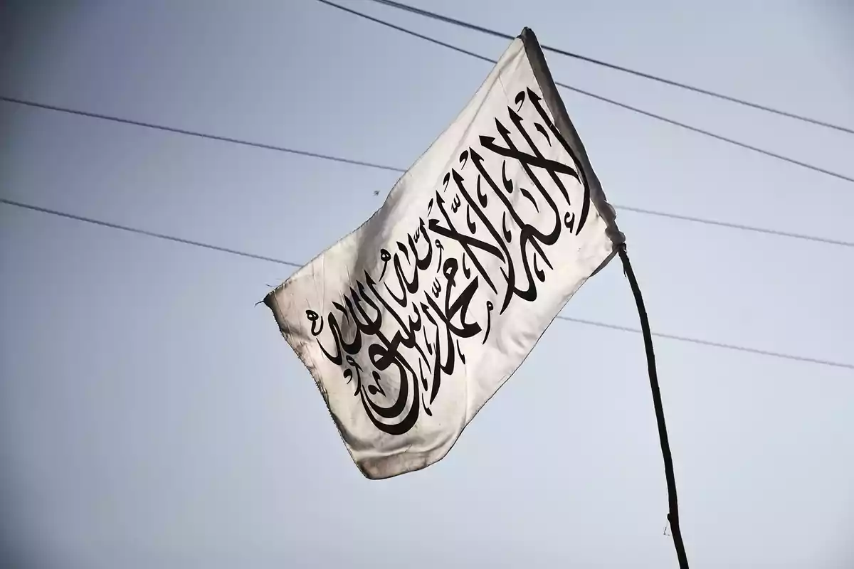 Una bandera blanca con inscripciones en árabe ondea en el aire bajo un cielo despejado.
