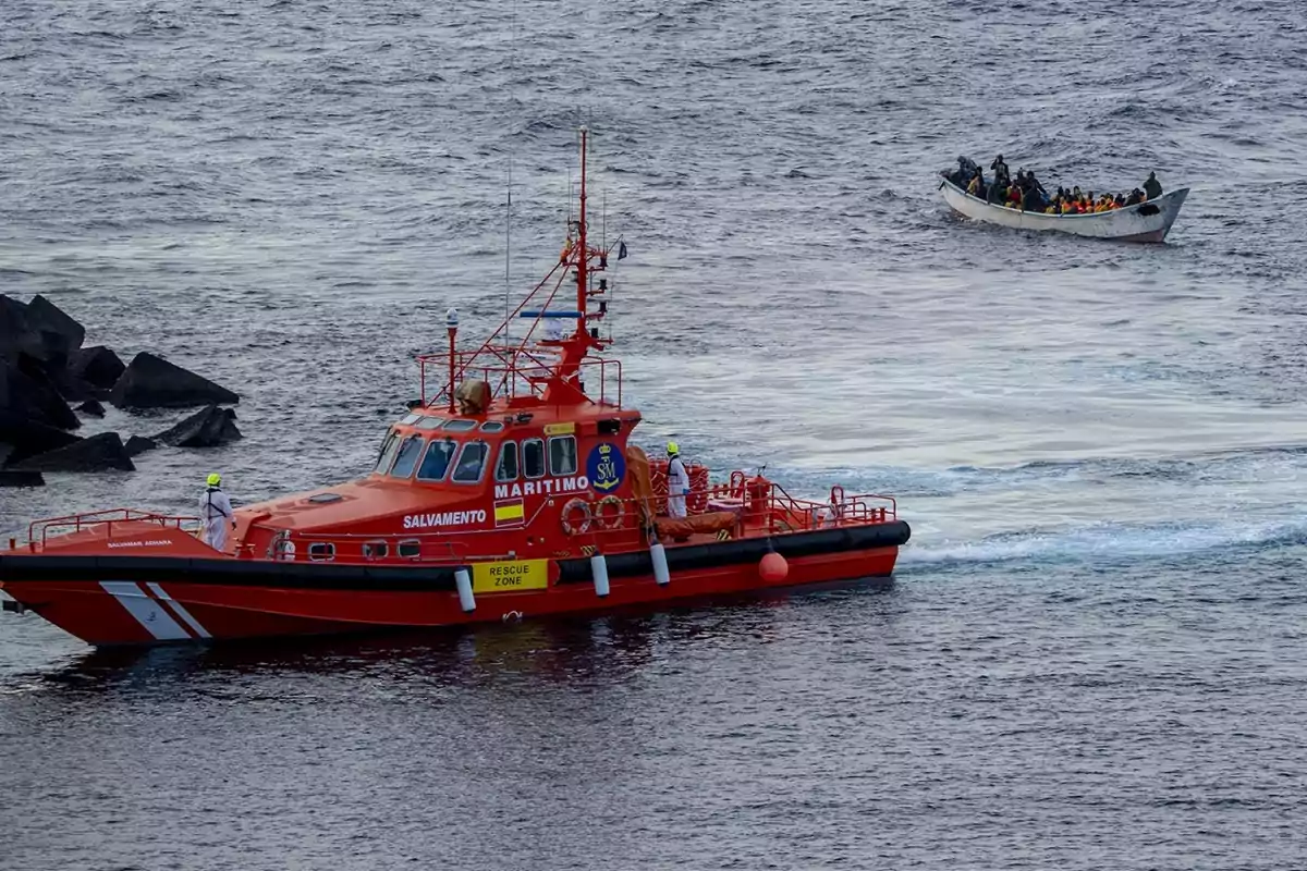 Un barco de rescate marítimo se acerca a una embarcación llena de personas en el mar Un barco de rescate marítimo se acerca a una embarcación llena de personas en el mar