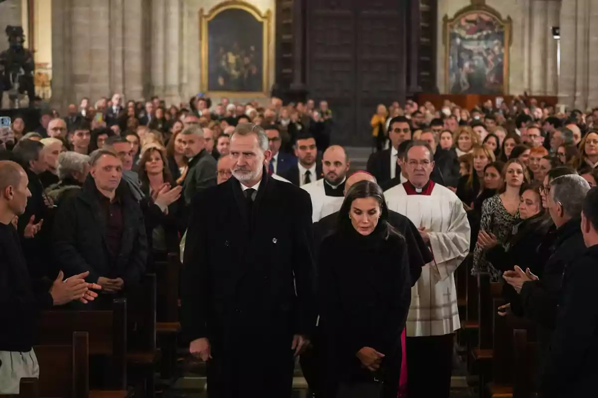 Personas caminando por el pasillo central de una iglesia rodeadas de una multitud de asistentes.