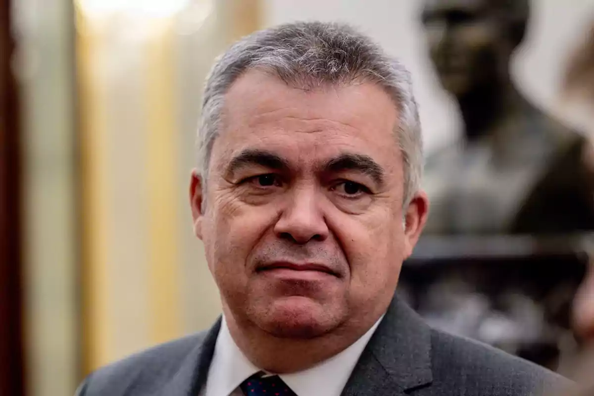 Hombre de cabello canoso y expresión seria vistiendo traje y corbata en un entorno interior elegante