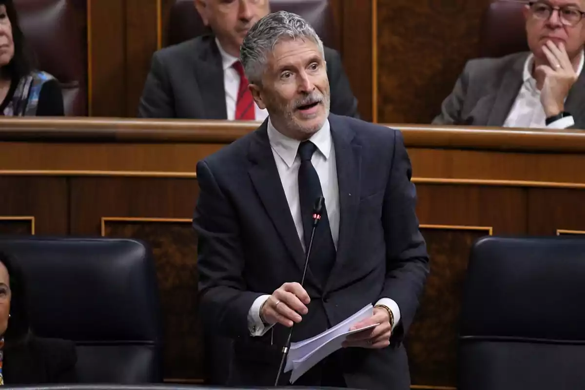 Un hombre de traje hablando en un parlamento con otras personas sentadas detrás de él.