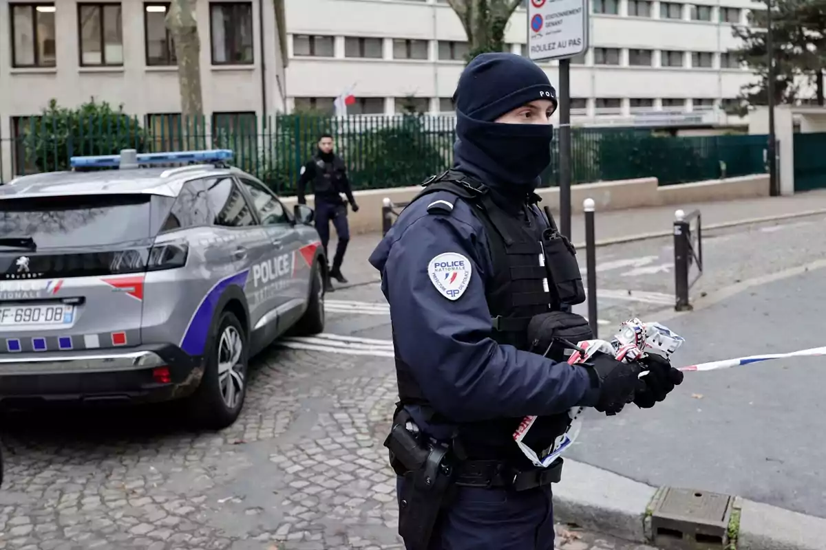 Policía francesa acordonando una zona en una calle urbana junto a un coche patrulla Policía francesa acordonando una zona en una calle urbana junto a un coche patrulla