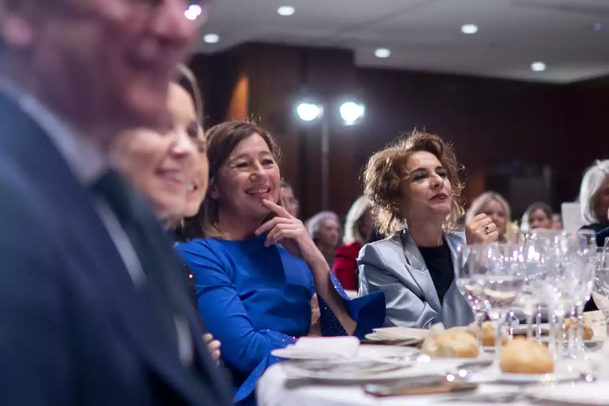 Personas sentadas en una mesa elegante durante un evento social, con copas y platos en primer plano.