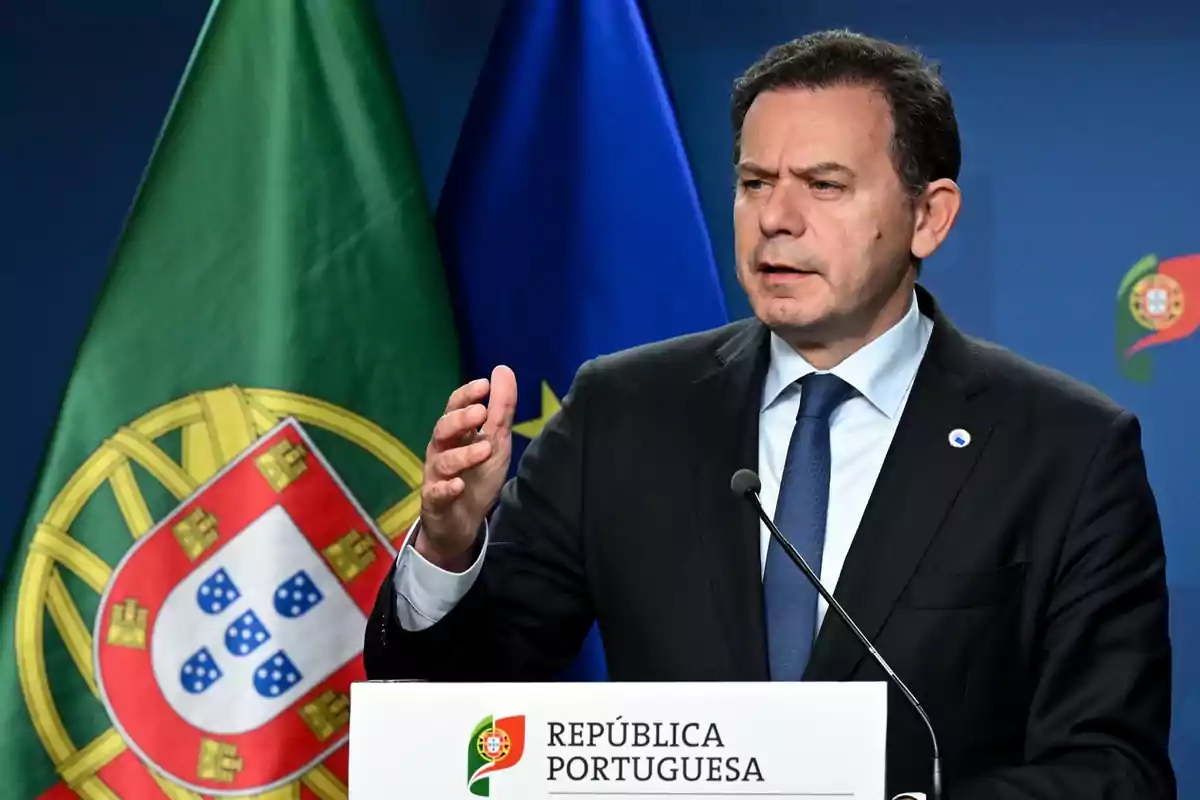 Un hombre en traje habla en un podio con la bandera de Portugal detrás.