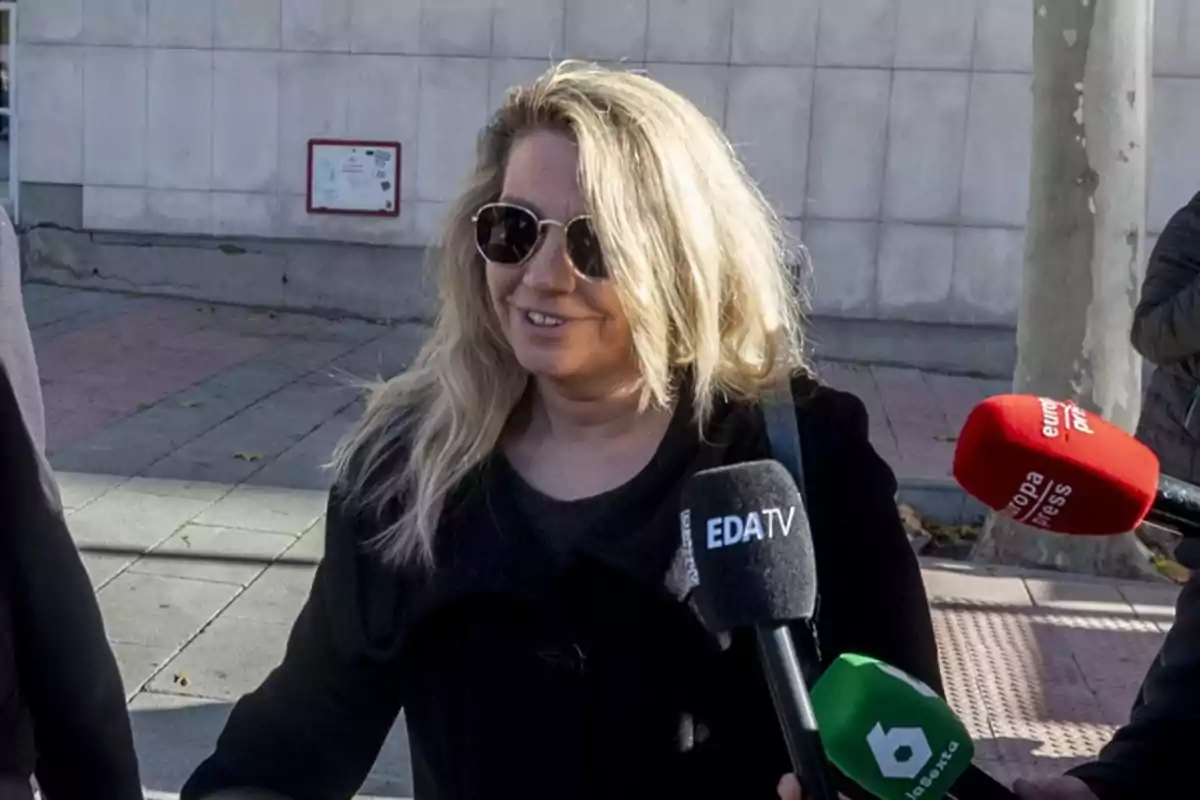 Una mujer con gafas de sol es entrevistada por varios medios de comunicación en la calle.