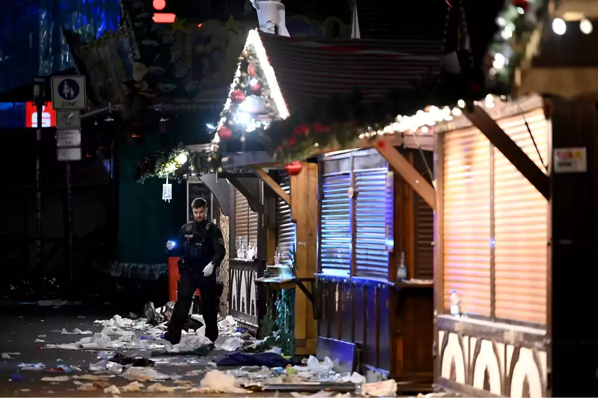 Un policía camina entre puestos de mercado navideño cerrados y rodeados de basura en la noche.