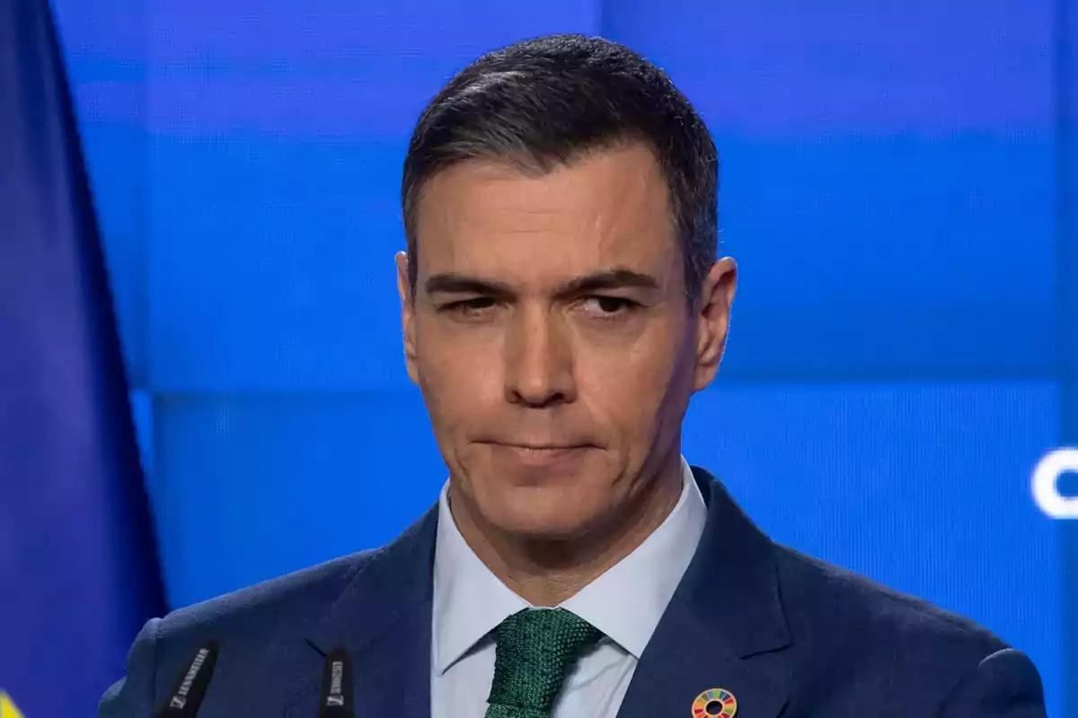 Hombre en traje azul con corbata verde frente a un fondo azul.