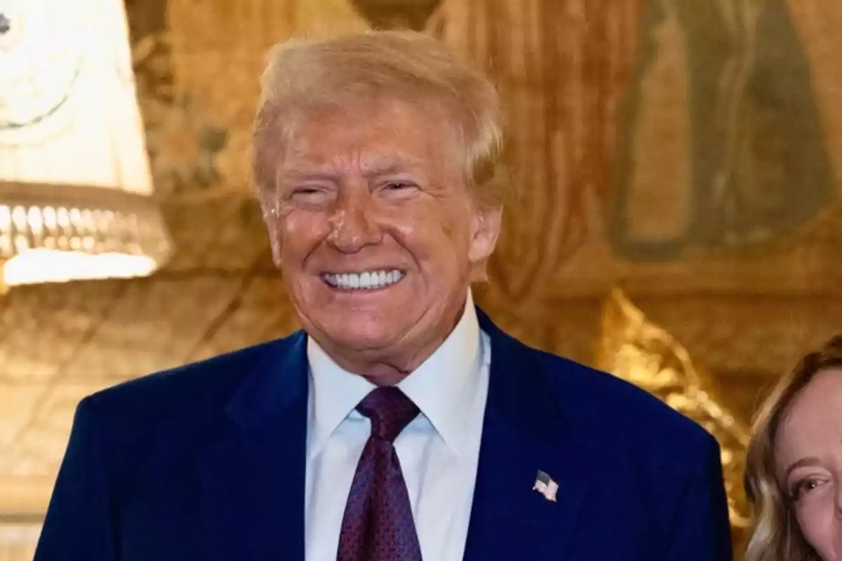 A smiling man in a dark suit and red tie in an elegant interior setting.