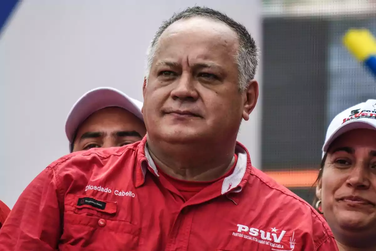 Un hombre con camisa roja y dos personas detrás, una de ellas con gorra blanca. Un hombre con camisa roja y dos personas detrás, una de ellas con gorra blanca.
