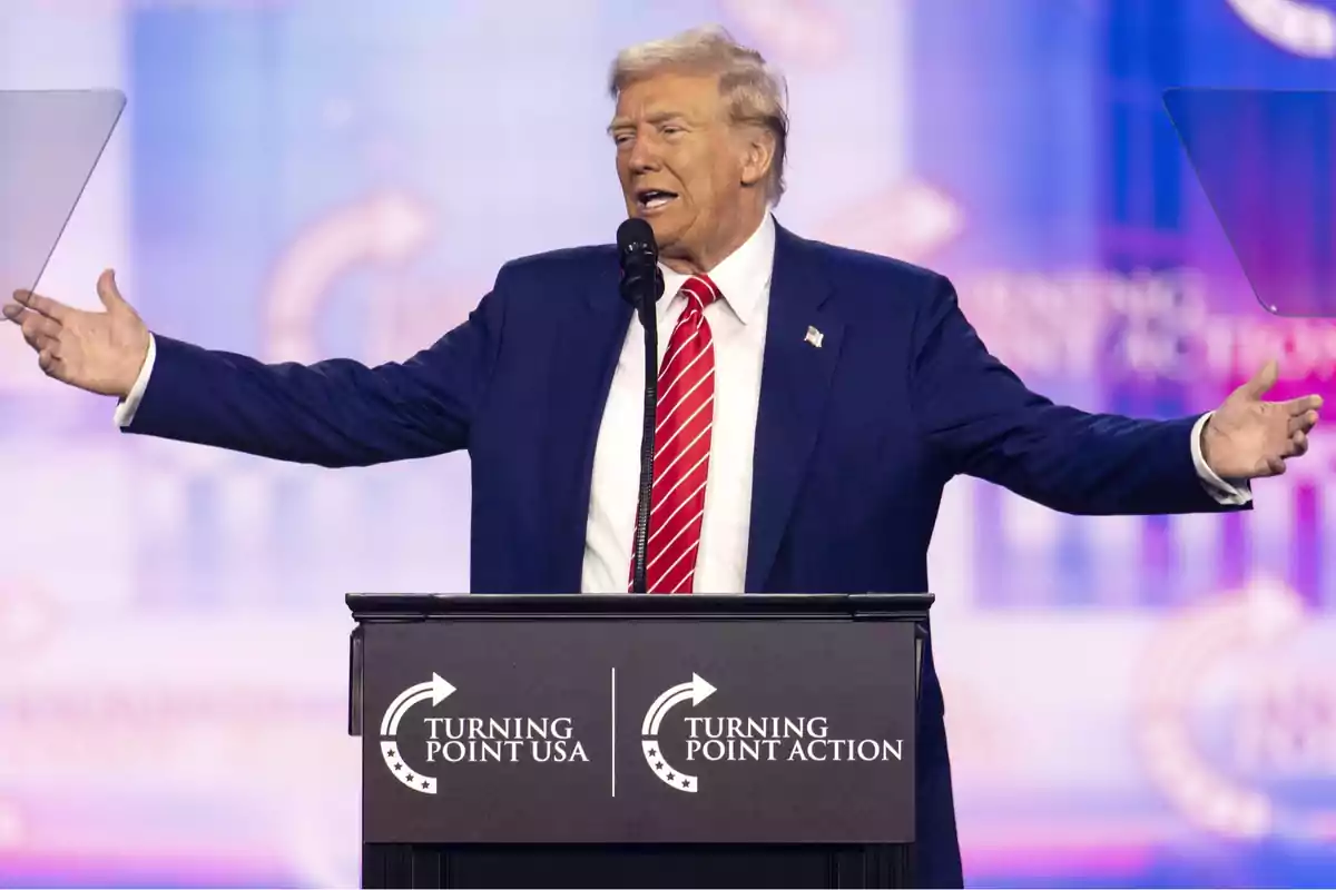 Un hombre de traje azul y corbata roja hablando en un podio con el logo de Turning Point USA. Un hombre de traje azul y corbata roja hablando en un podio con el logo de Turning Point USA.