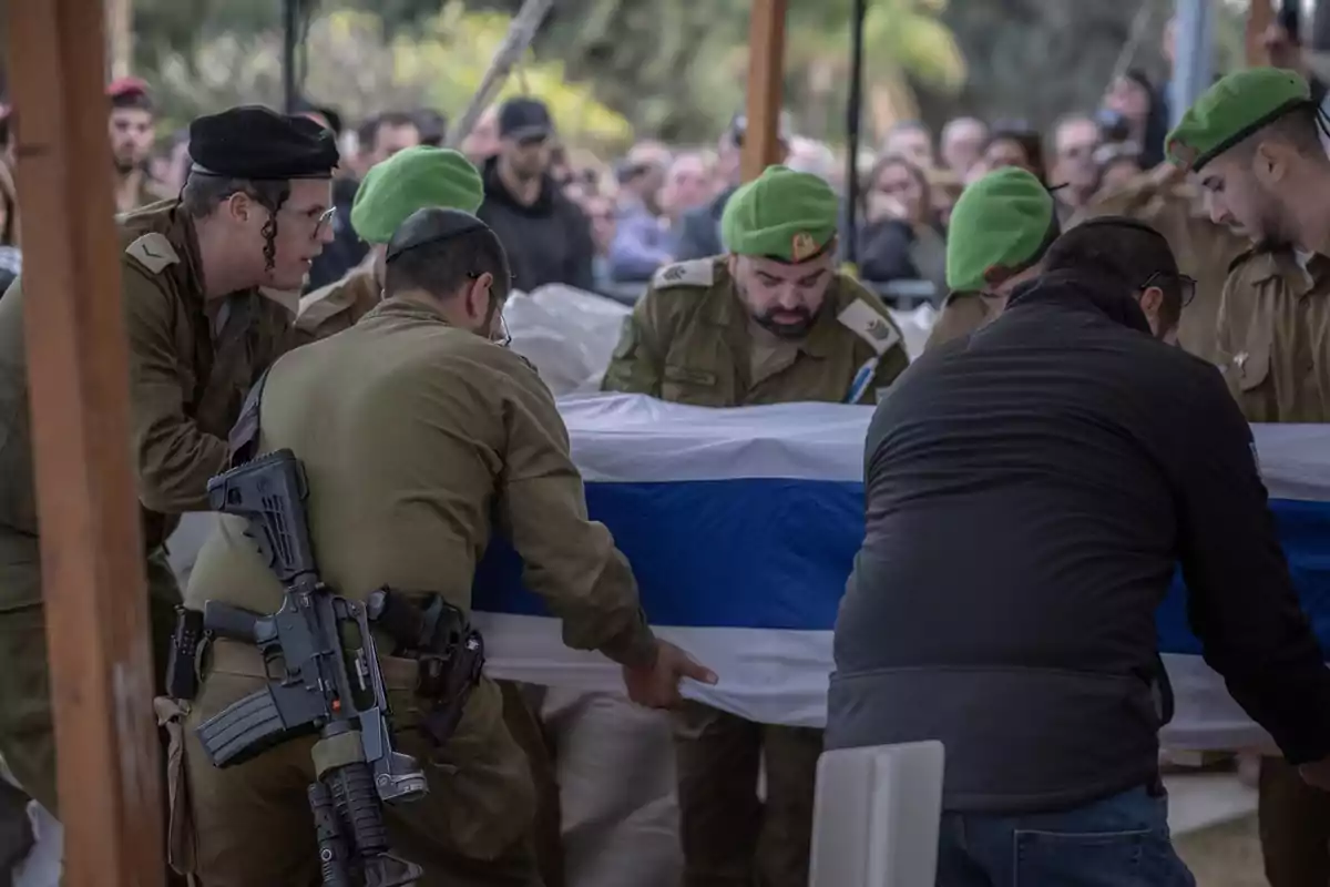 Un grupo de soldados con boinas verdes lleva un ataúd cubierto con una bandera en una ceremonia al aire libre, rodeados de personas.