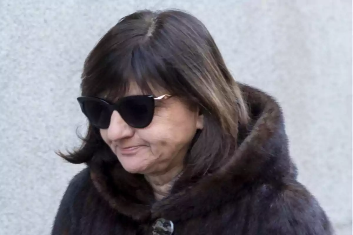 Woman in sunglasses and fur coat walking outdoors.