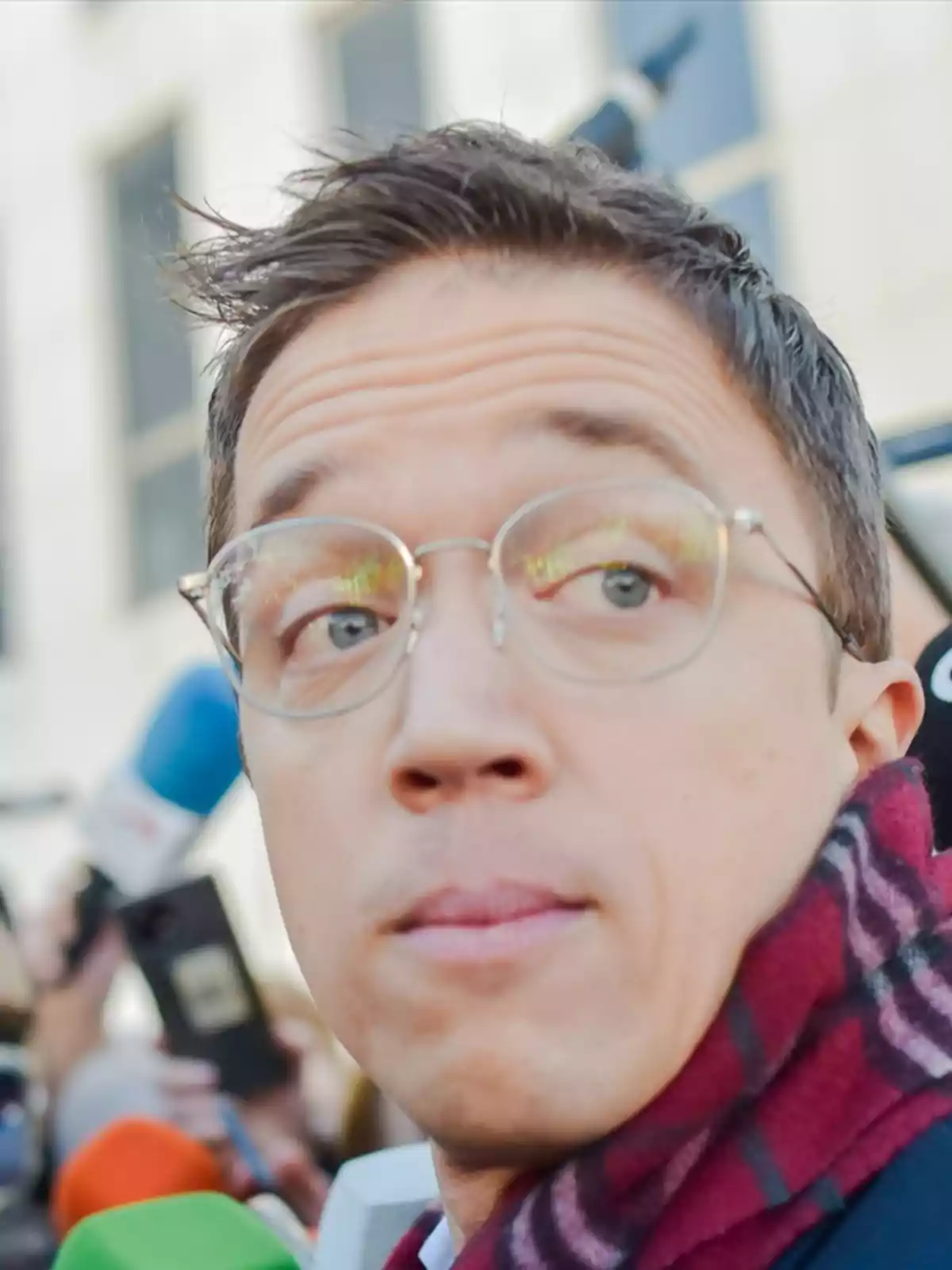 A man with glasses and a scarf in an urban setting.