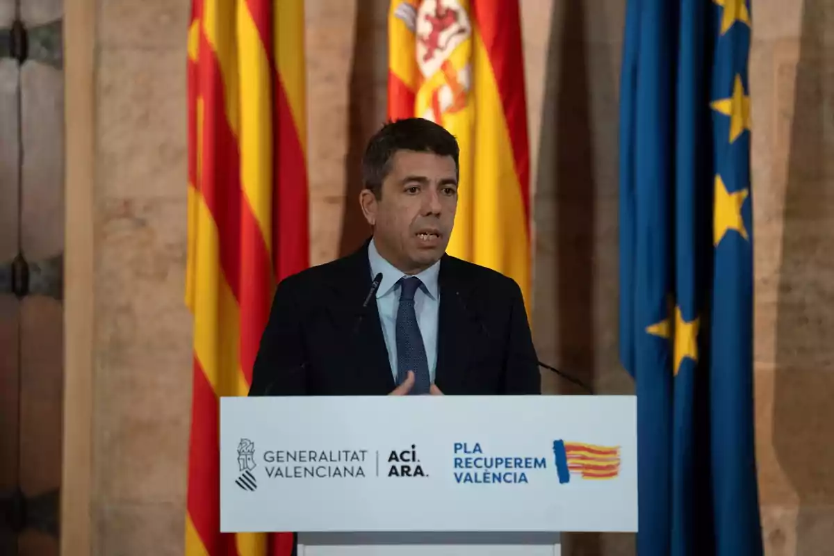 A man speaking at a podium with flags in the background.