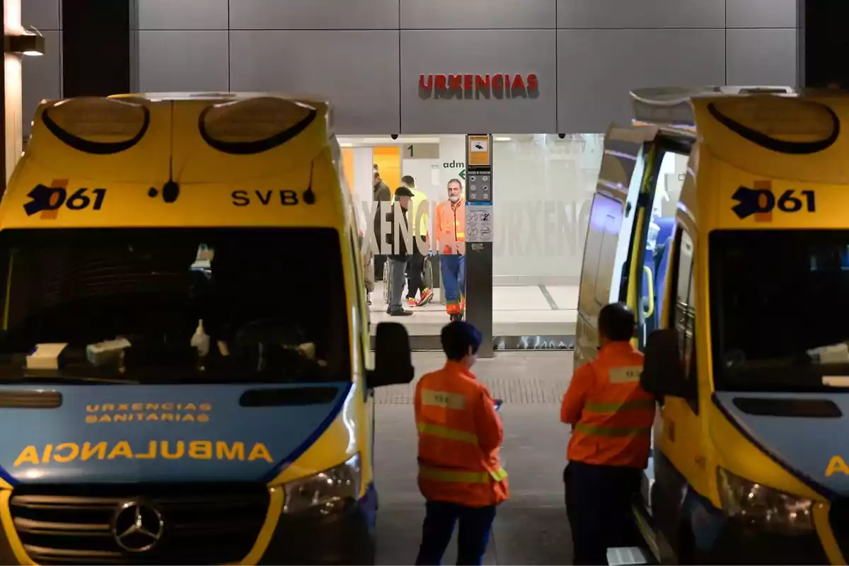 Ambulancias estacionadas frente a la entrada de urgencias de un hospital, con personal médico de pie cerca de las ambulancias.