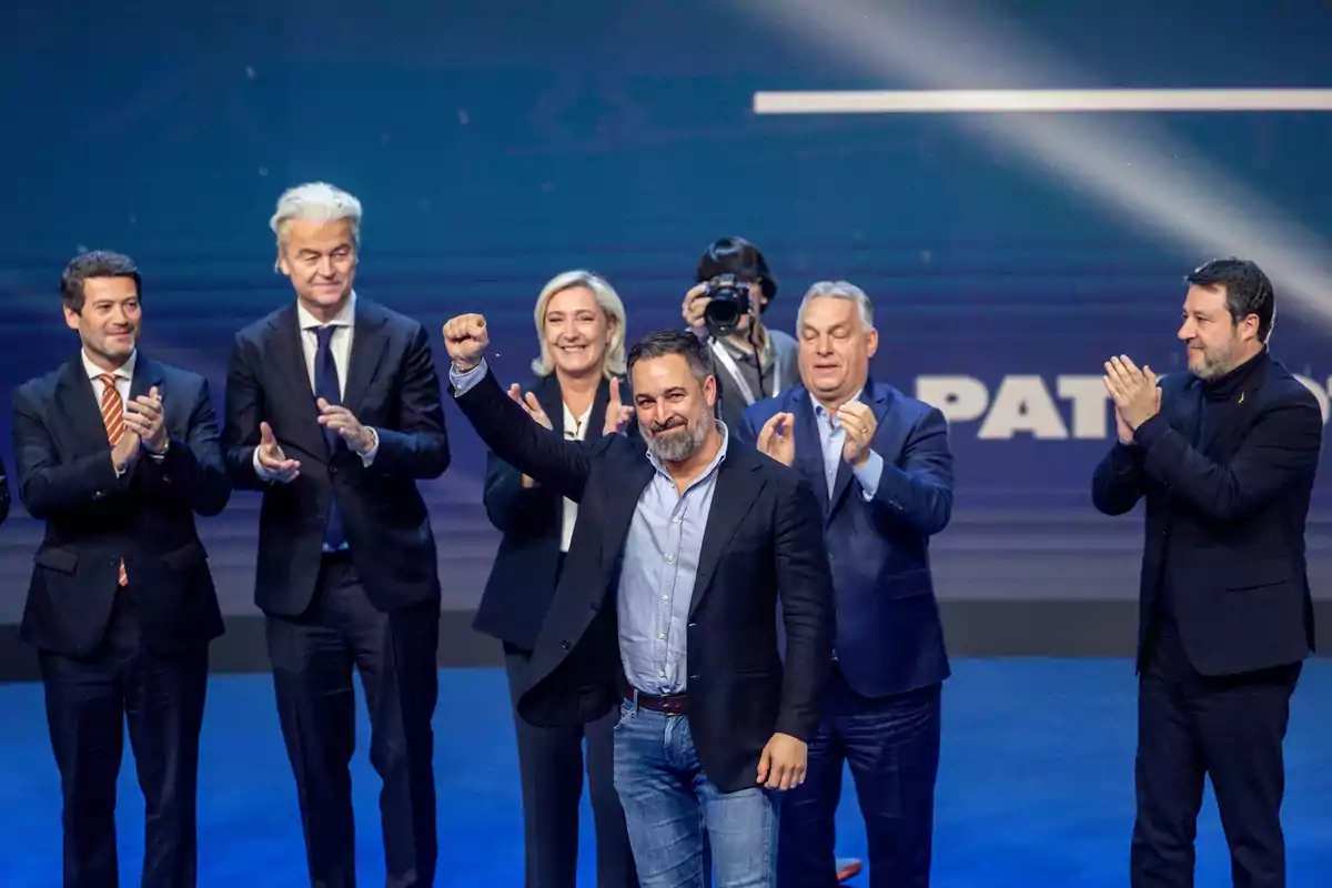 A group of people on a stage applauding while a man in the center raises his fist.