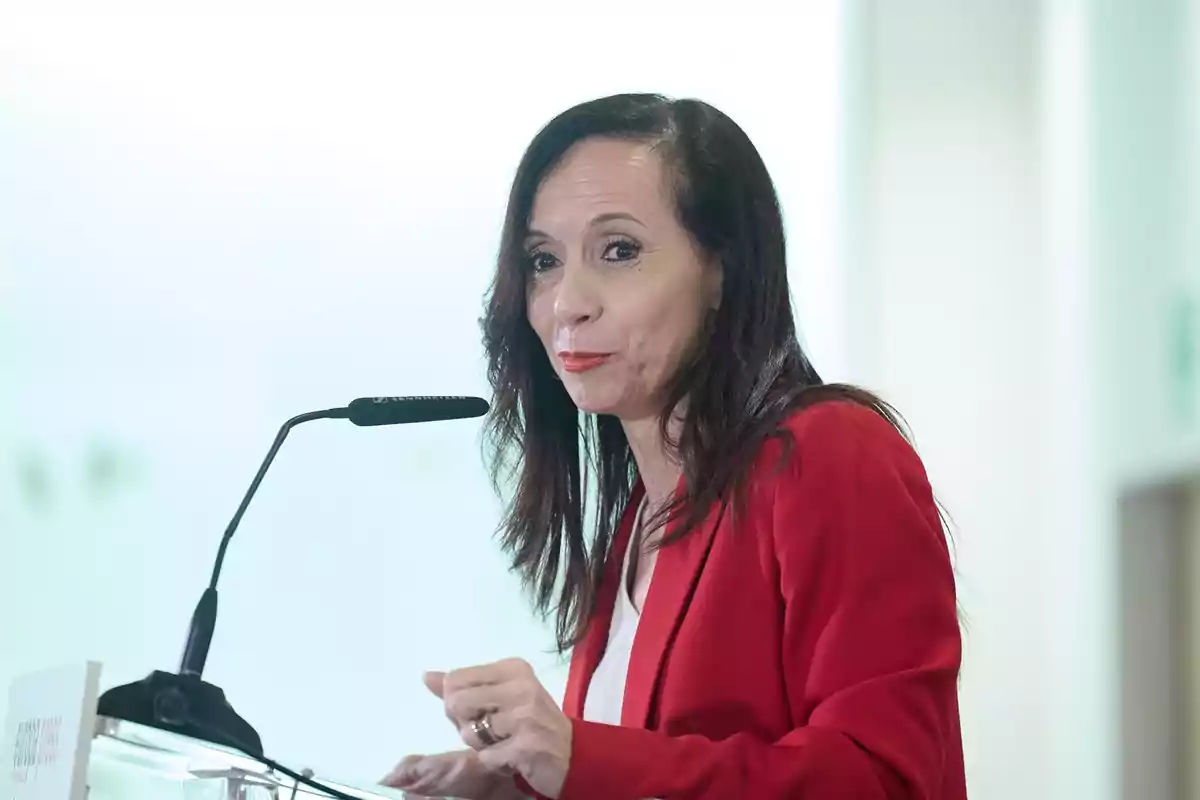 Una persona con chaqueta roja hablando en un micrófono durante un evento. Una persona con chaqueta roja hablando en un micrófono durante un evento.