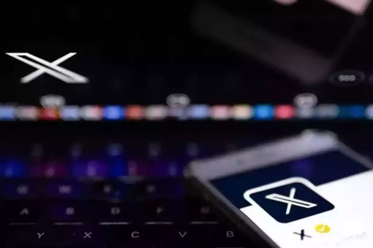 Un teléfono móvil mostrando un logotipo de "X" en la pantalla con un teclado de computadora en el fondo.