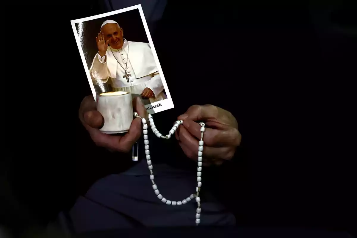 A person holds a candle, a rosary, and a photograph of a religious figure dressed in white.