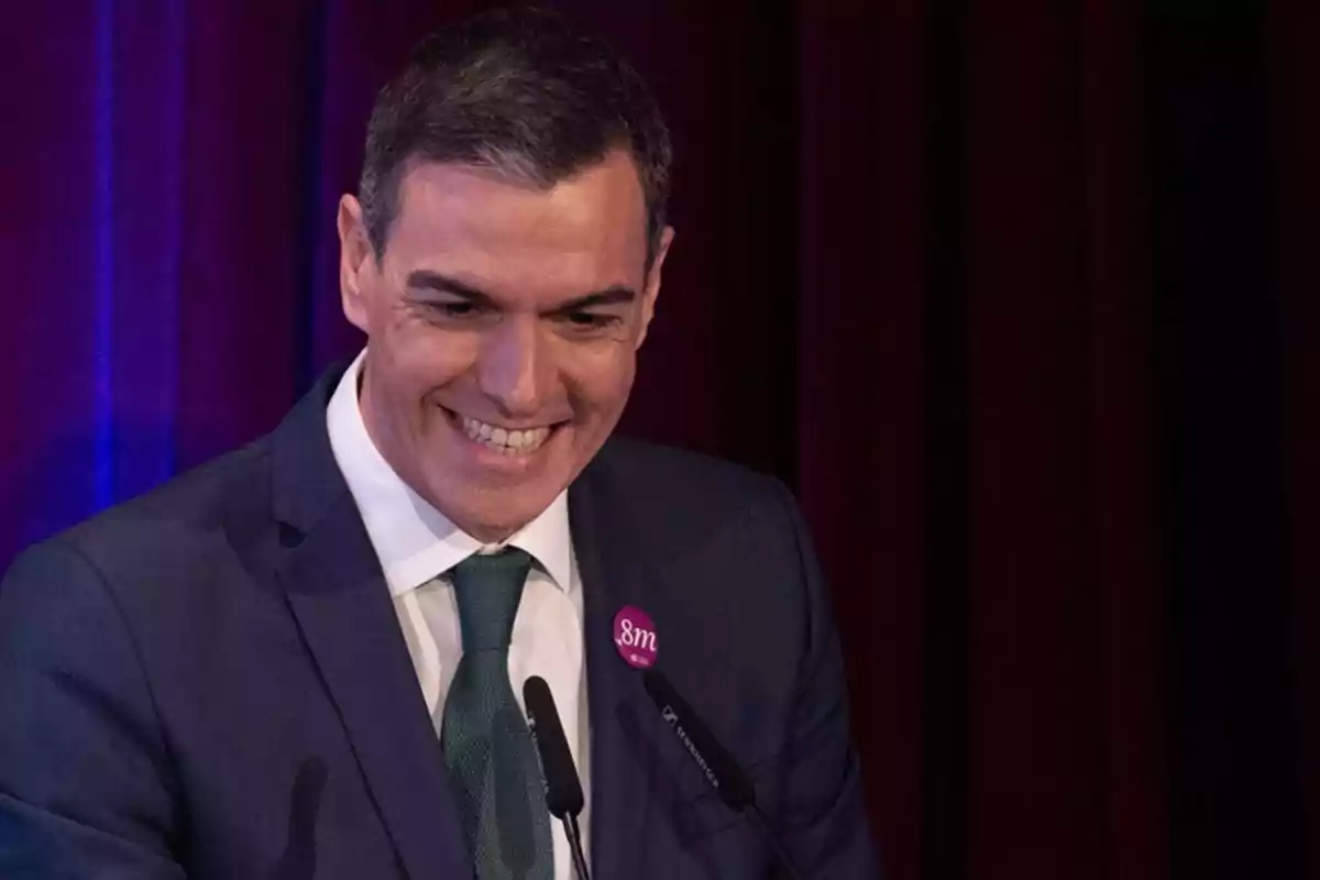 Un hombre sonriente en un evento con fondo de cortinas oscuras.