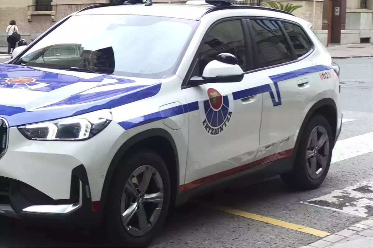 Un coche de policía blanco con detalles azules y rojos estacionado en una calle urbana.