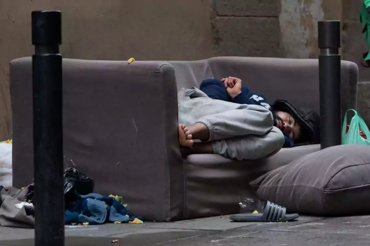 Persona durmiendo en un sofá en la calle rodeada de algunas pertenencias y basura Persona durmiendo en un sofá en la calle rodeada de algunas pertenencias y basura