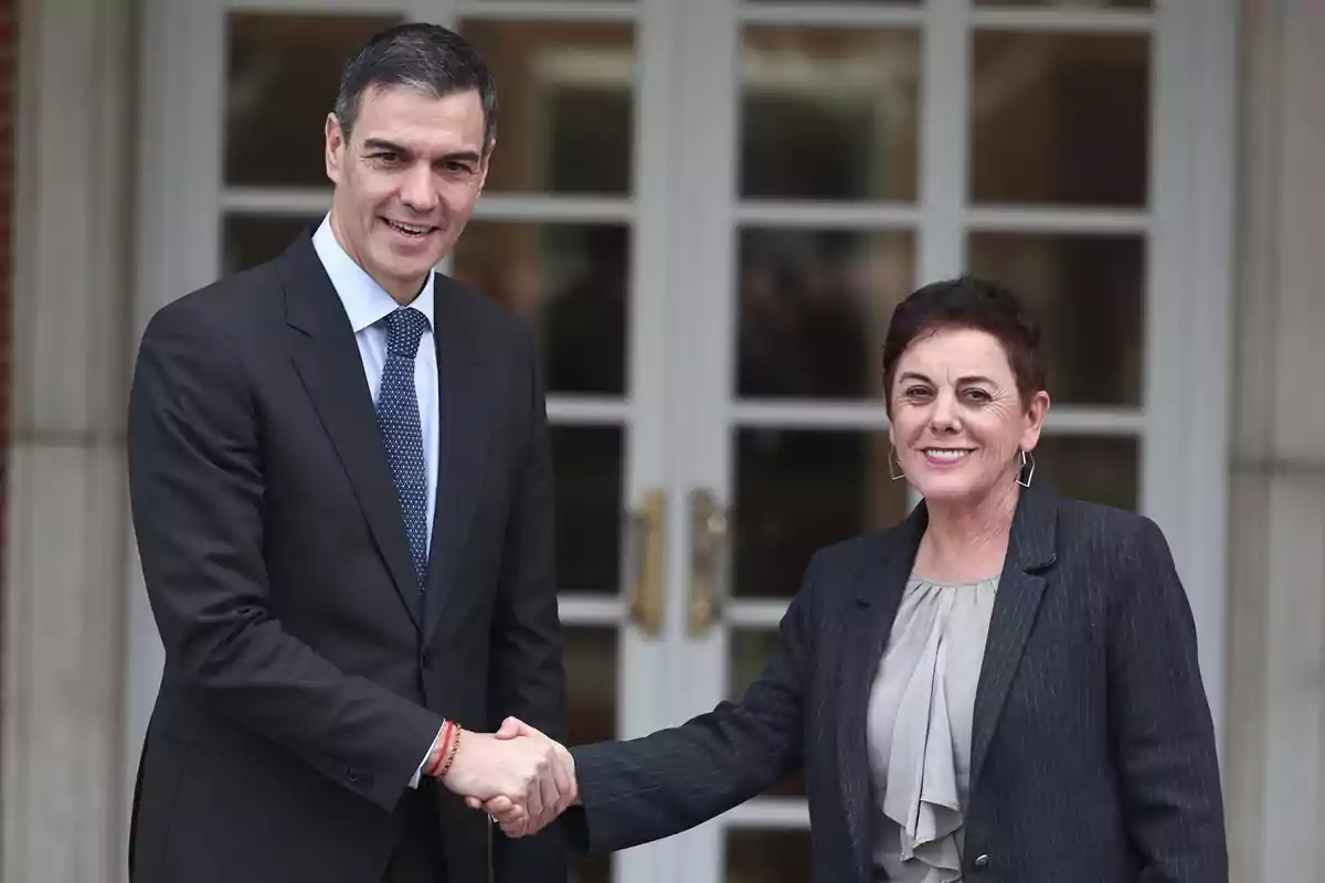 Dos personas dándose la mano frente a una puerta de vidrio.